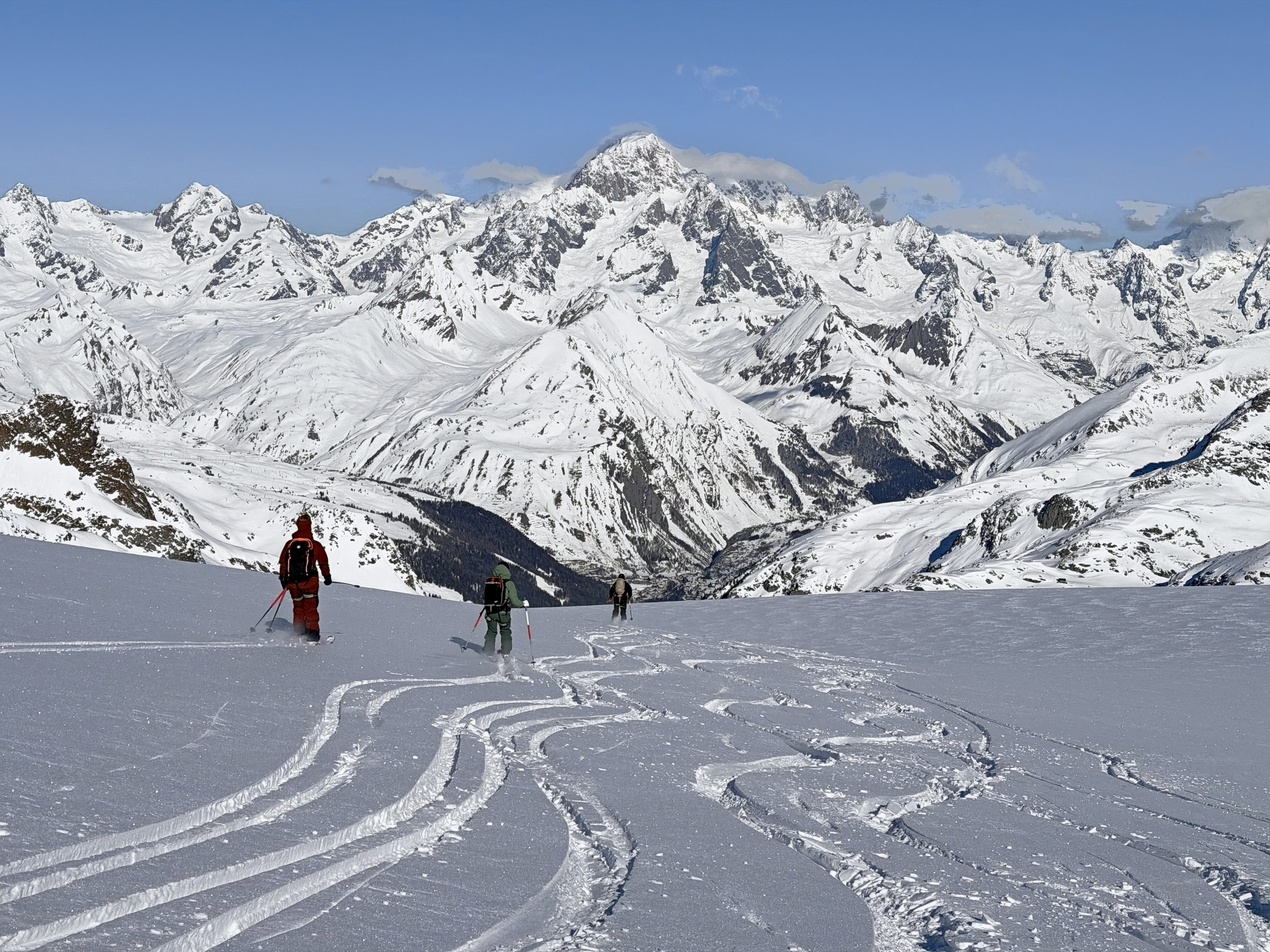 Drei Skifahrer im verspurten Pulverhang bei La Thuile, vor einem großen vergletscherten Massiv