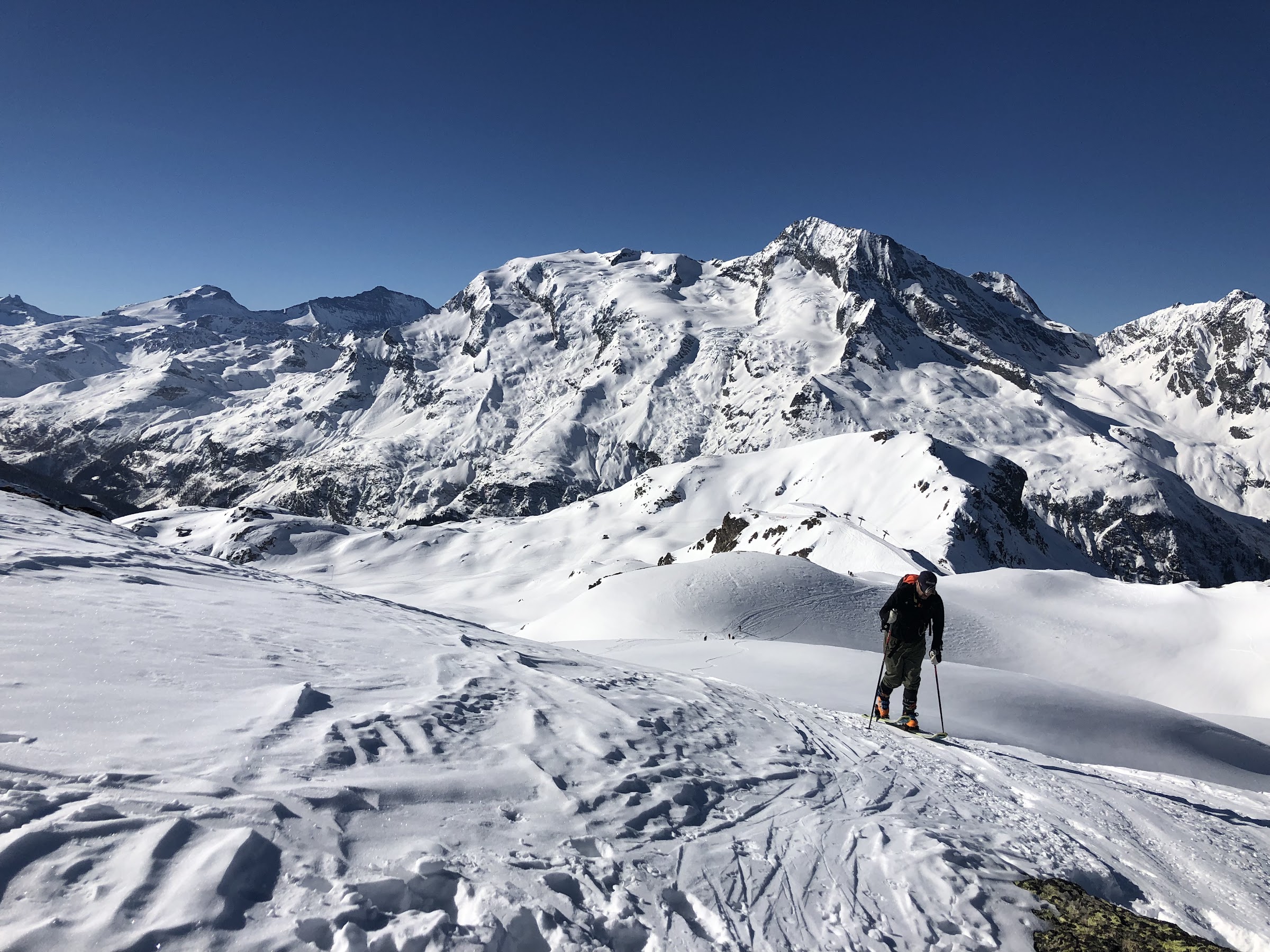Skier skinning up a snowy crest with a large snow-covered massif behind