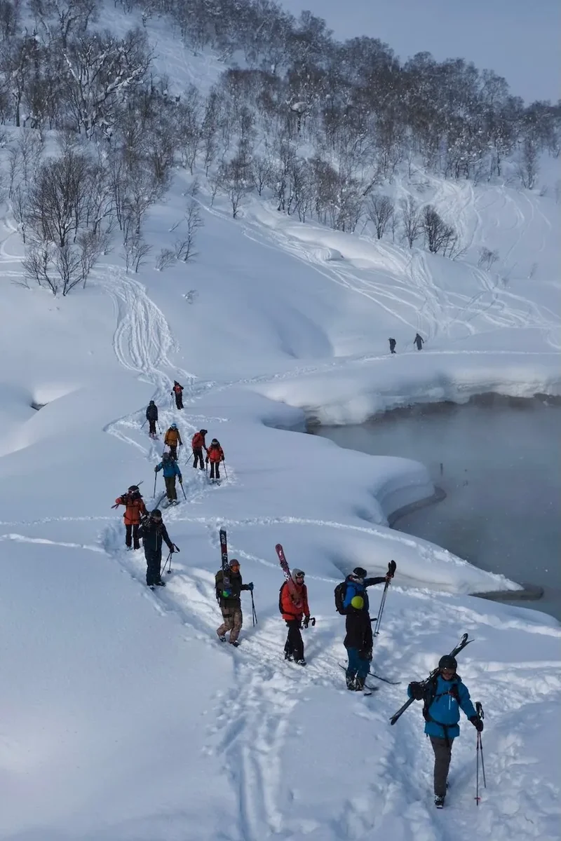 Eine Reihe Skifahrer steigt mit Fellen an einem verschneiten Fluss entlang auf