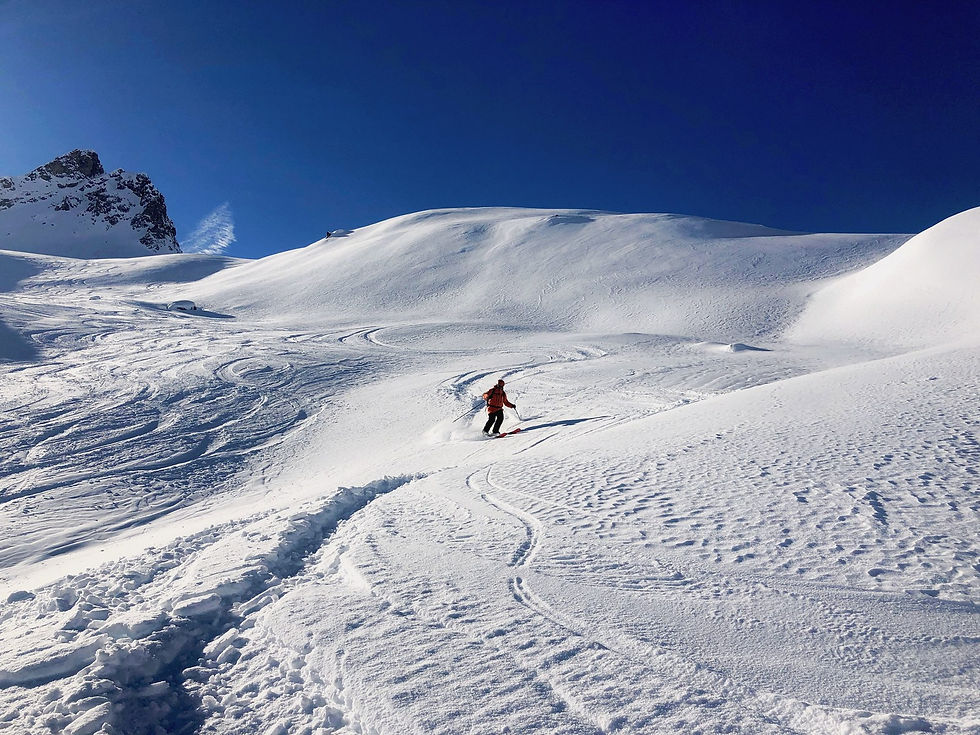Un skieur descend une grande combe enneigée de Val d’Isère, ses traces dessinées dans la neige sous un ciel bleu profond