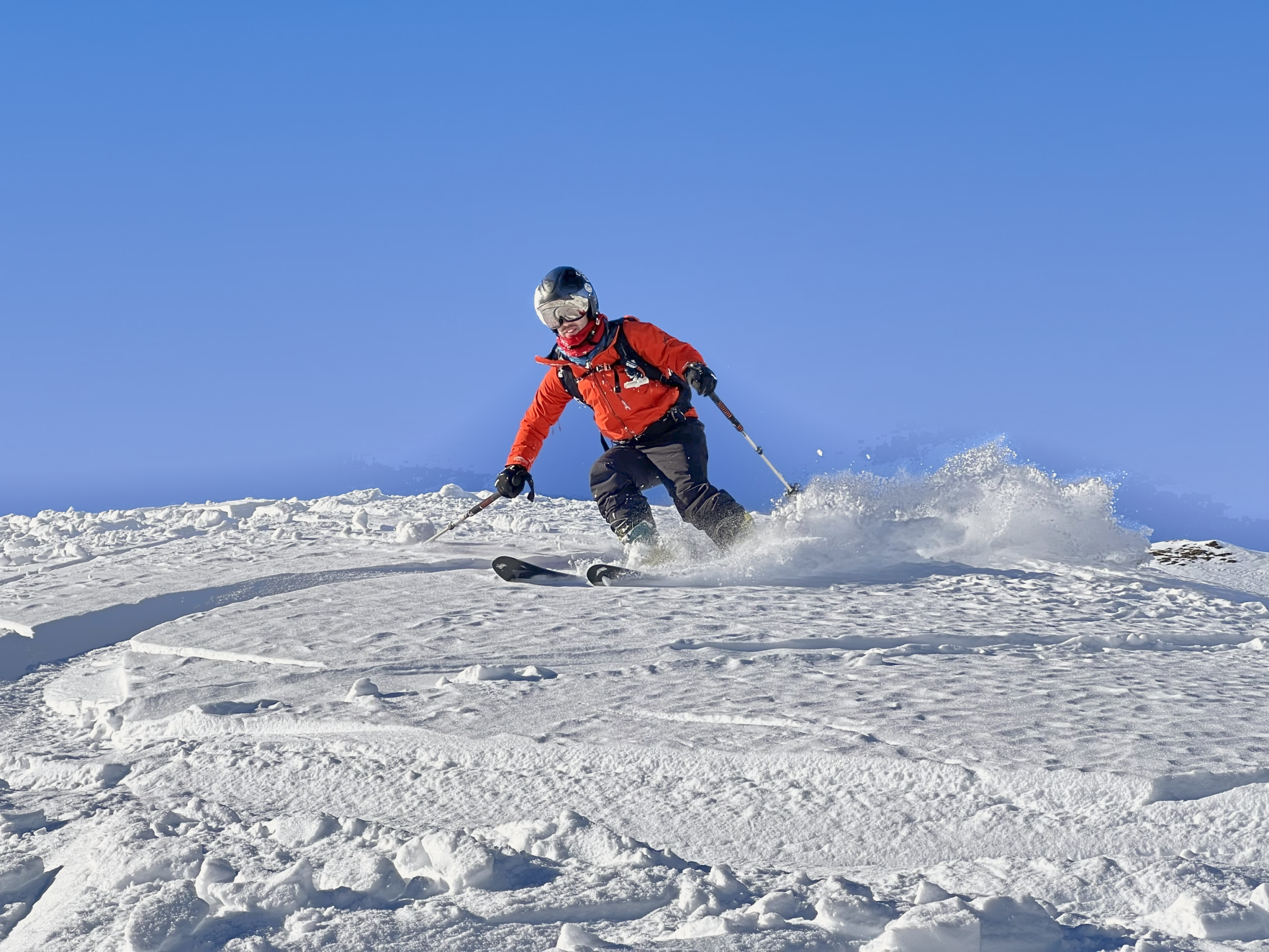 Private ski tuition in Val d'Isère: a skier in an orange jacket turning in powder under a clear blue sky