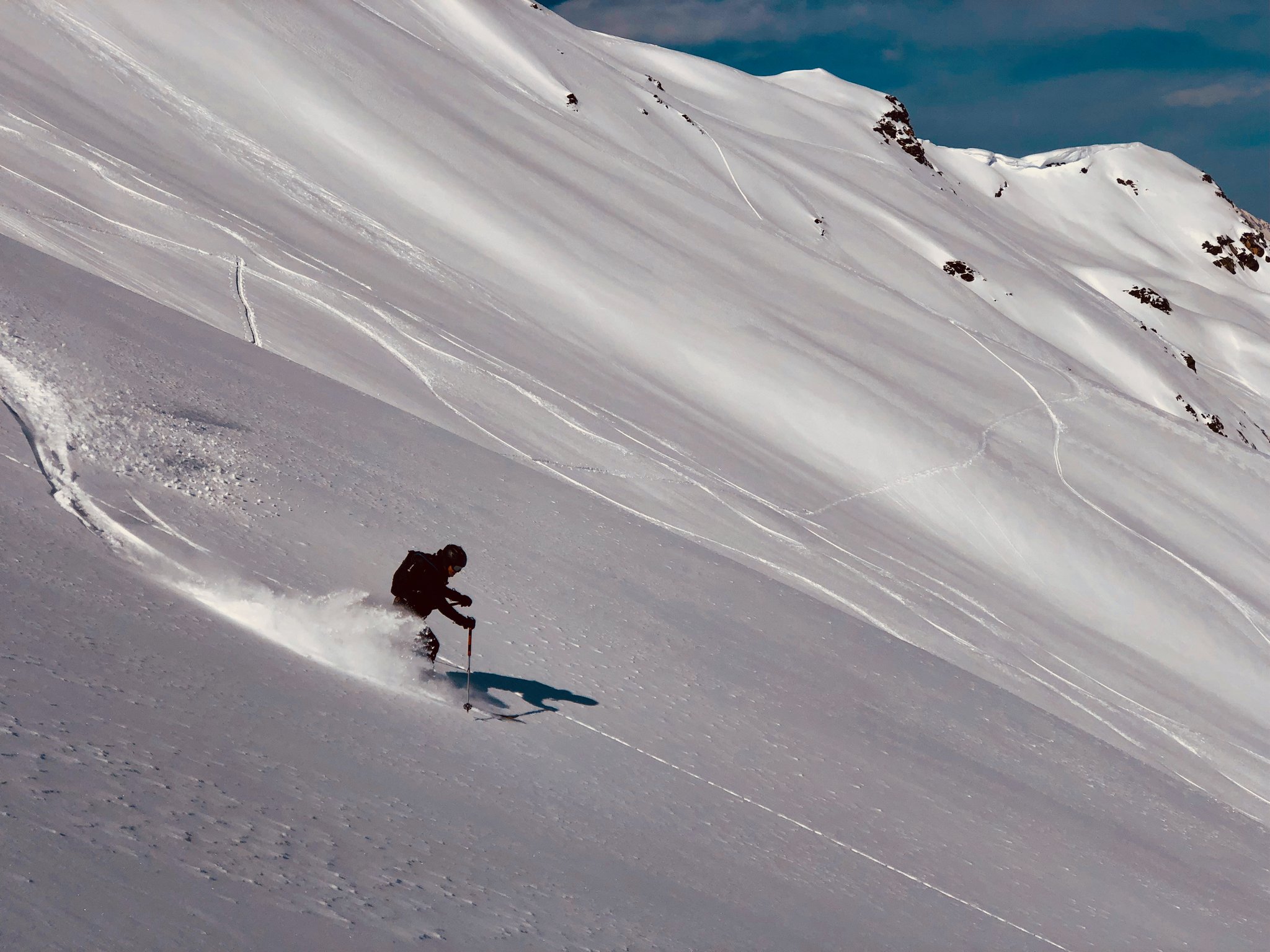 Ein einzelner Skifahrer zieht Schwünge im Pulverschnee auf einem weiten, sonnigen Hang abseits der Piste