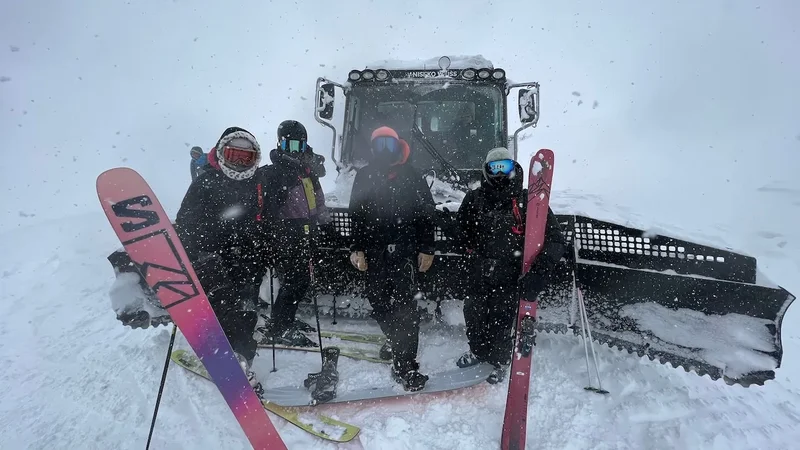 Eine lachende Gruppe Skifahrer vor einer Pistenraupe, bei Schneefall