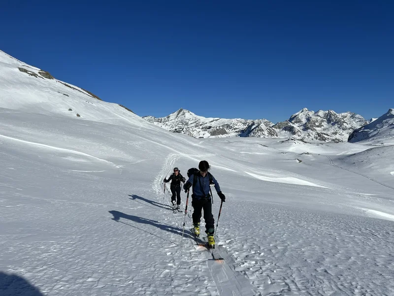 Deux skieurs de rando en montée dans un vaste cirque, ciel bleu