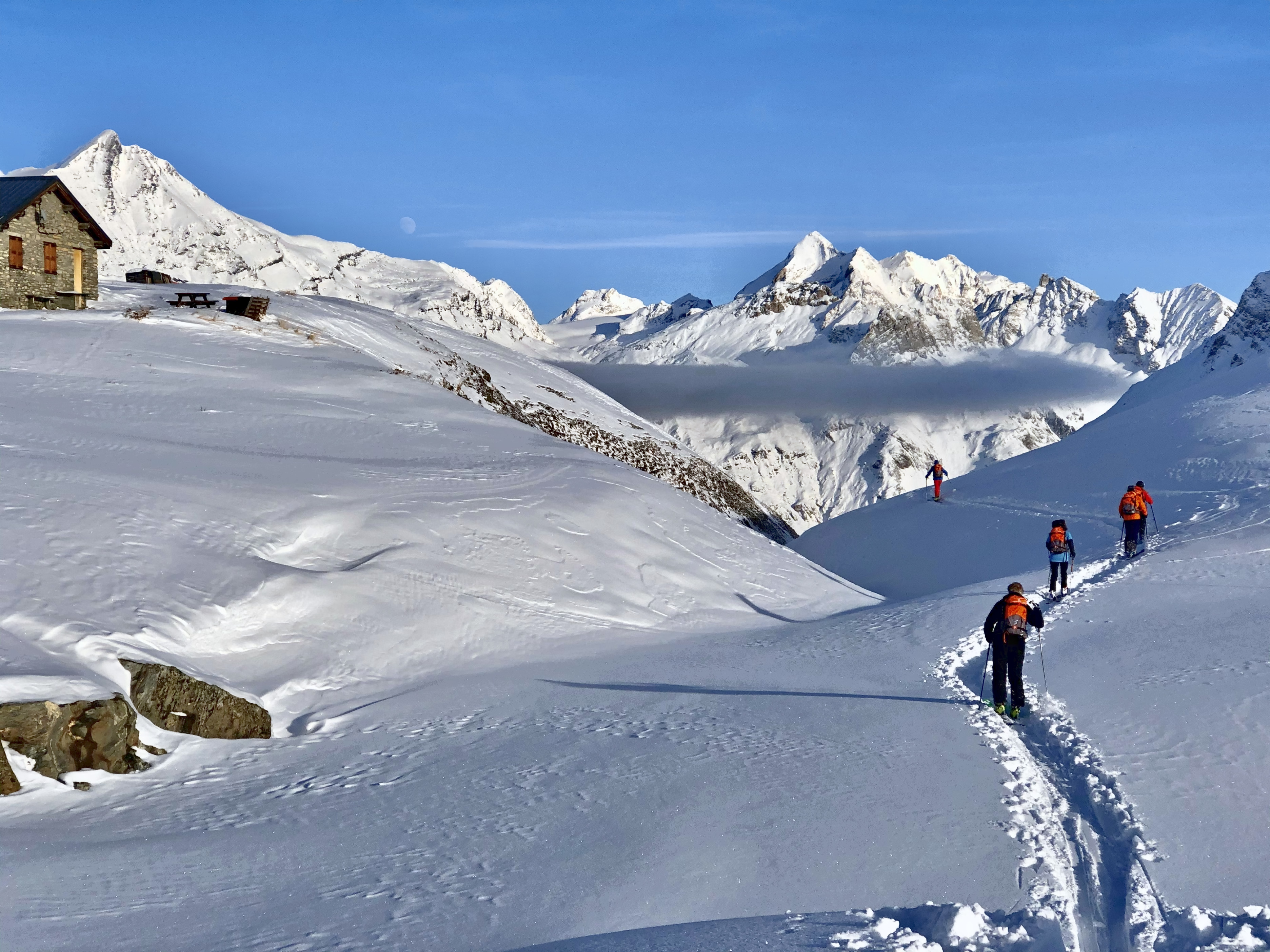 Skitourengruppe im Gänsemarsch auf einer Spur, dahinter ein Wolkenmeer und Gipfel