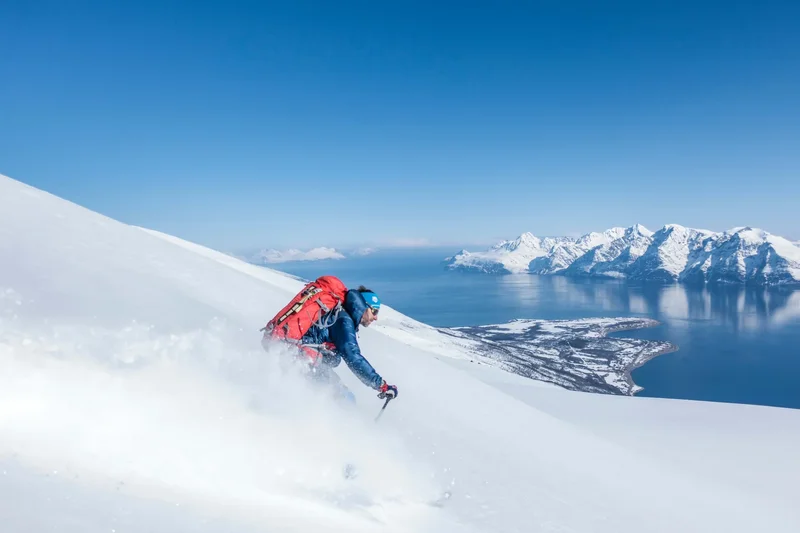 A skier in powder facing the fjord and the peaks, Bodø Alps, Norway