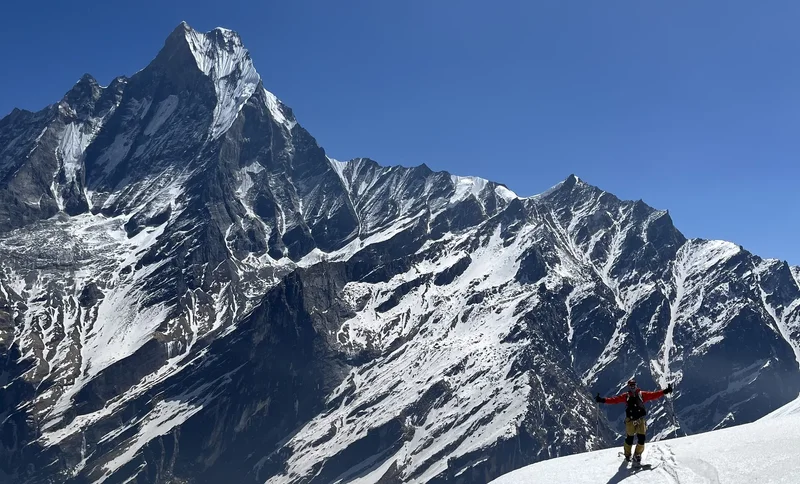 Der Machapuchare über einem Skifahrer mit ausgebreiteten Armen im Schnee, tiefblauer Himmel