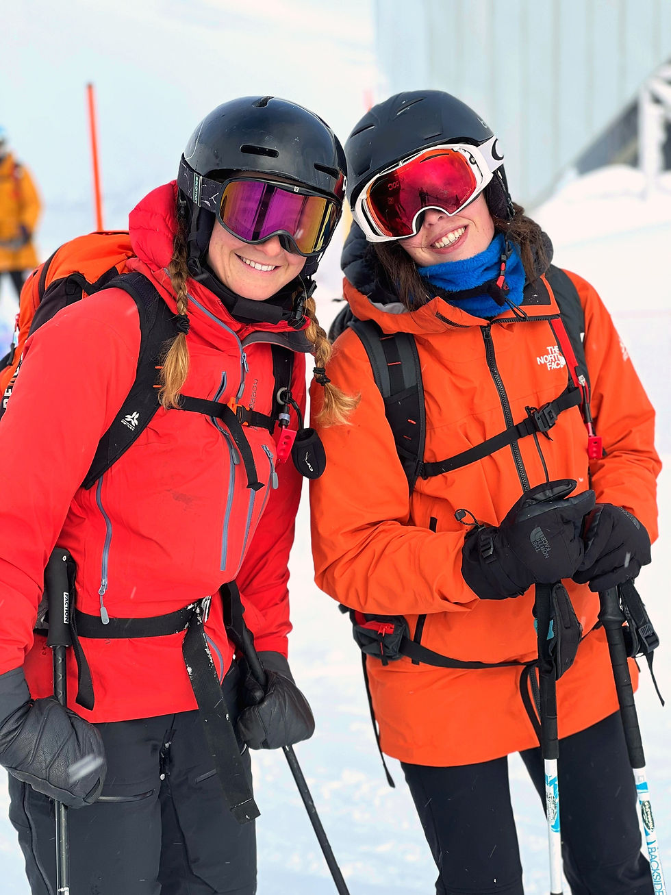 Deux skieuses en vestes rouge et orange sourient côte à côte, masque sur le casque