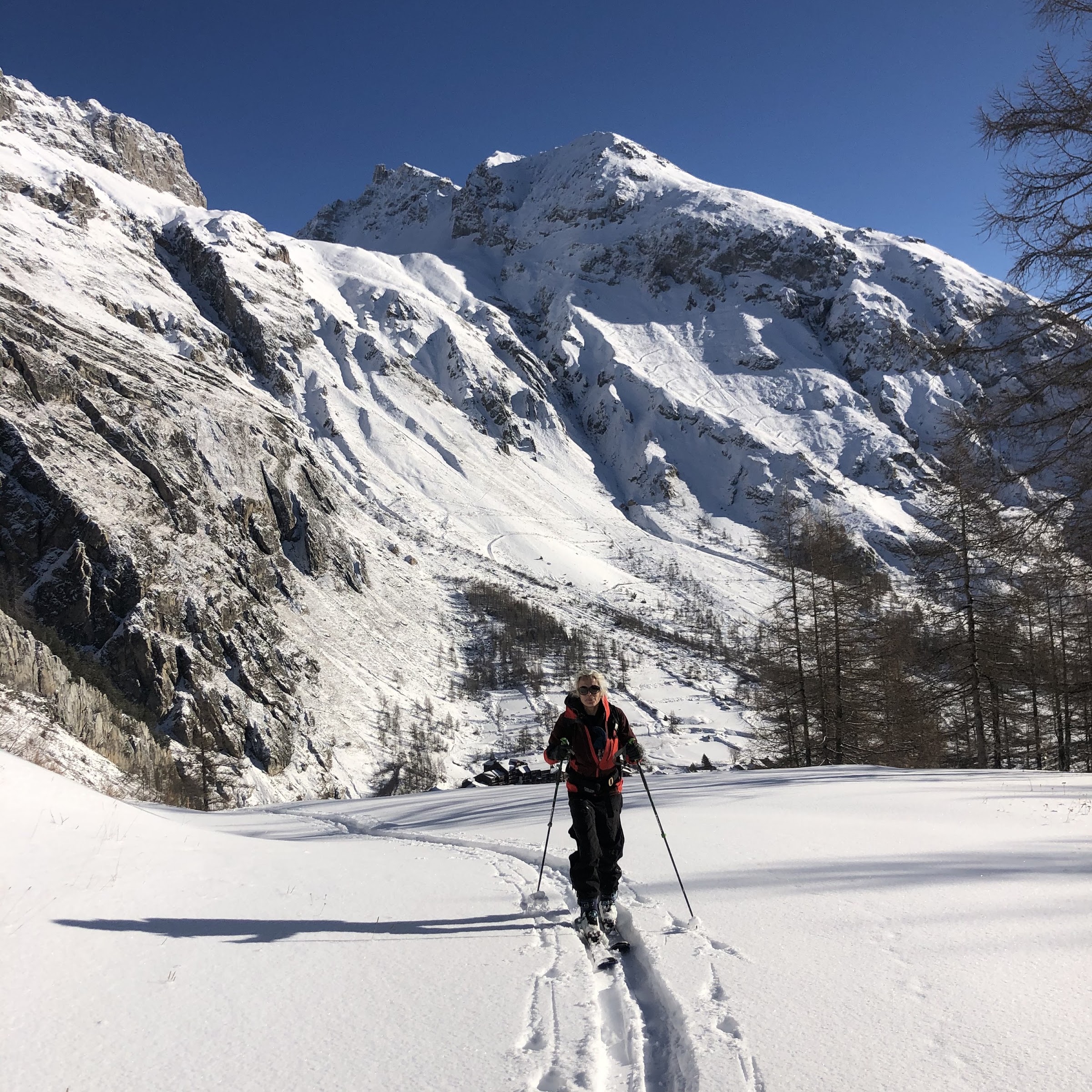 Skitourengeher beim Aufstieg mit Fellen in einem Tal mit Lärchen unter hohen verschneiten Wänden
