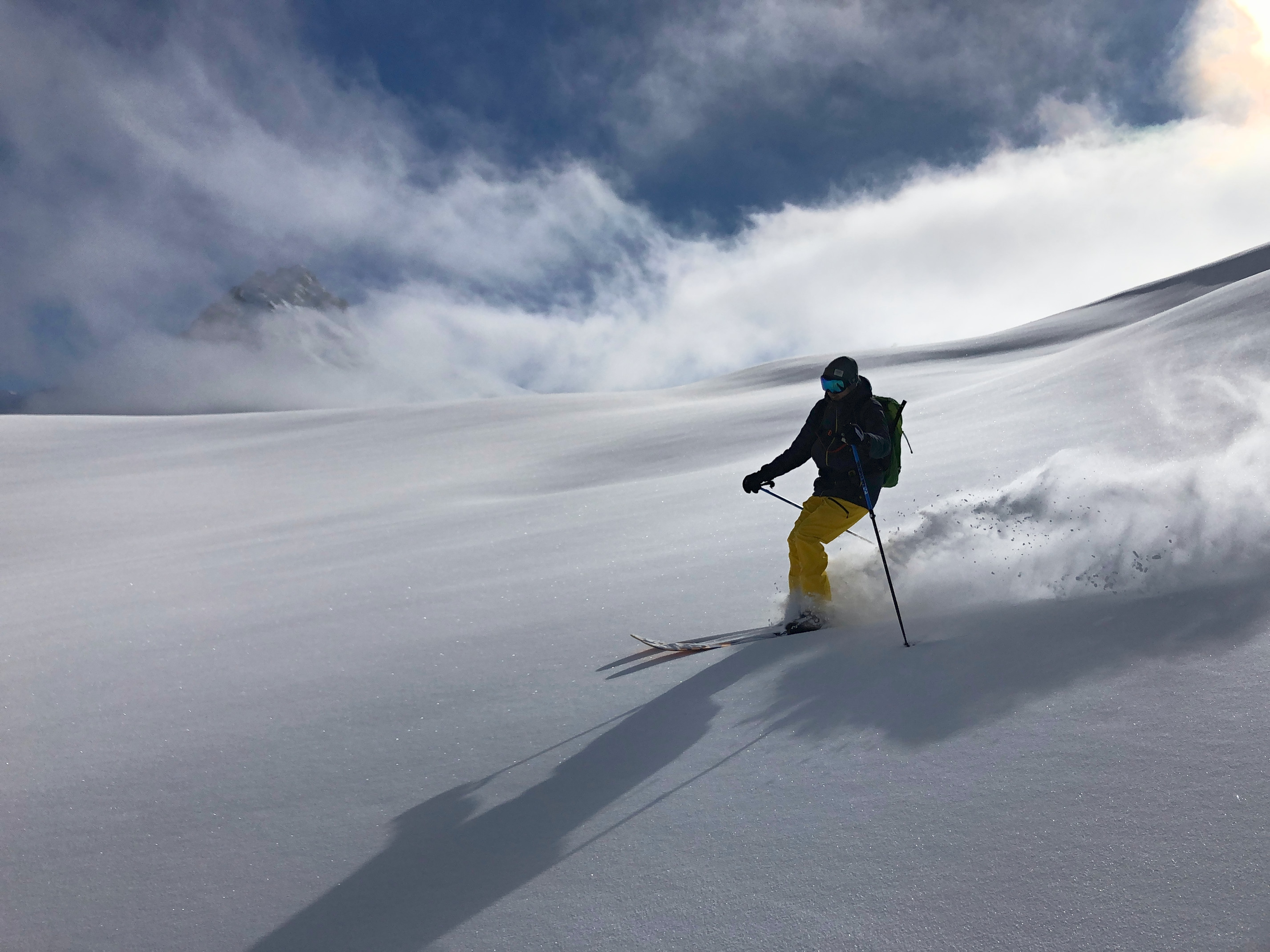 Ski hors-piste à Val d'Isère : skieur en pantalon jaune qui soulève la poudreuse dans une grande pente vierge