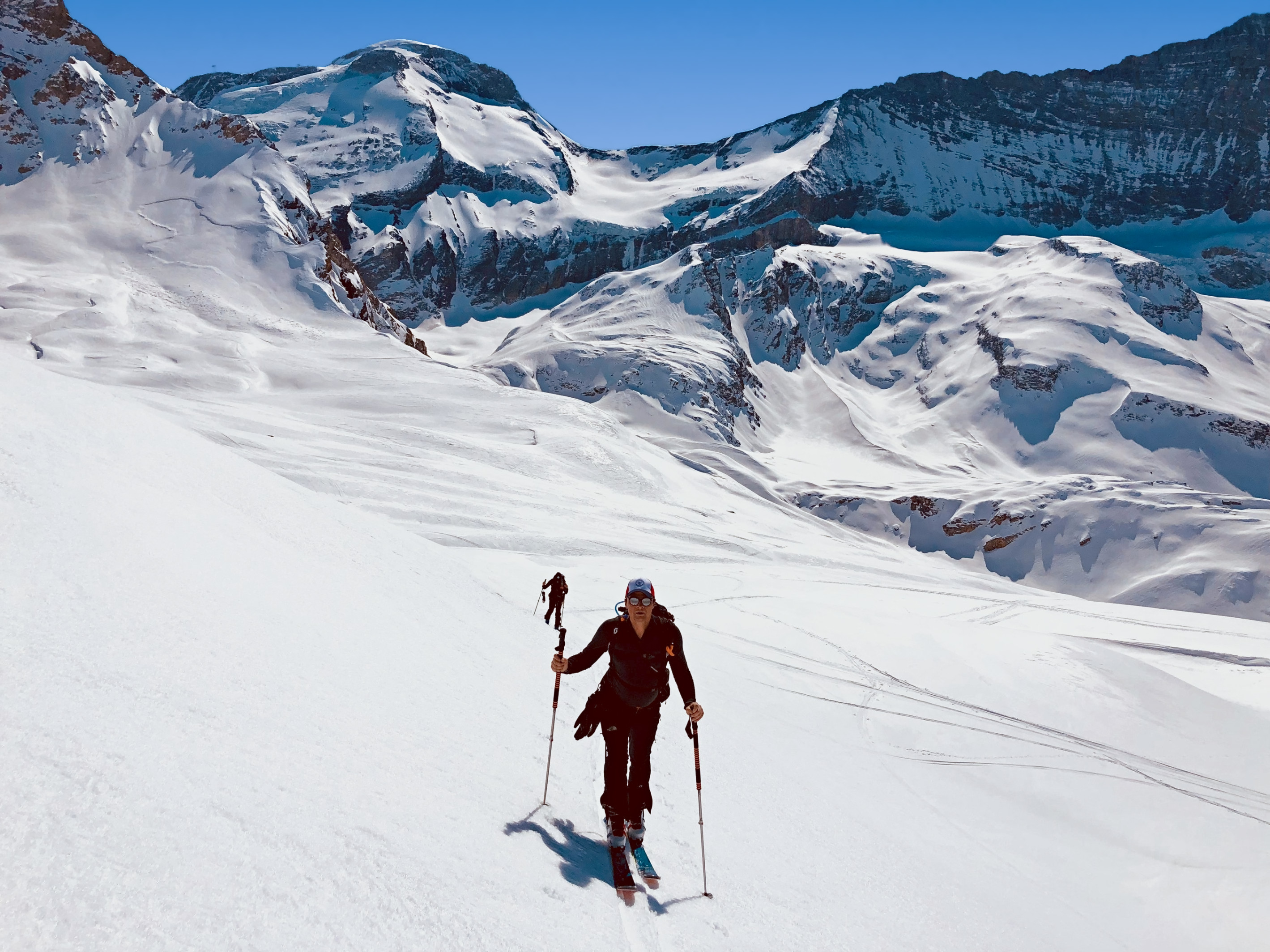 Tourengeher beim Aufstieg mit Fellen auf einem weiten Schneefeld, dahinter Gletscher und Gipfel