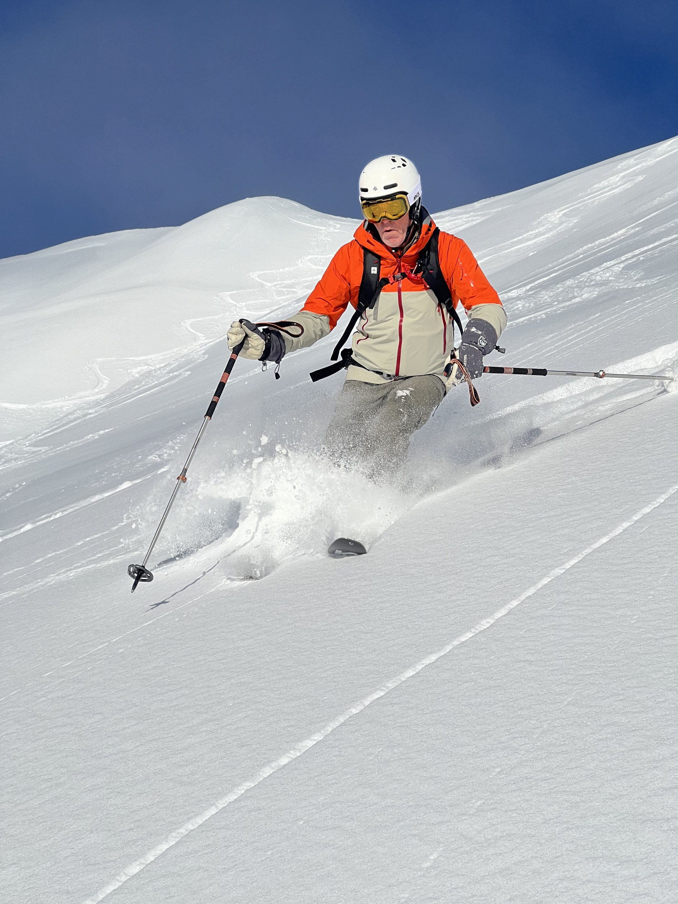 Skier in a white helmet turning in soft, light snow next to a fresh track