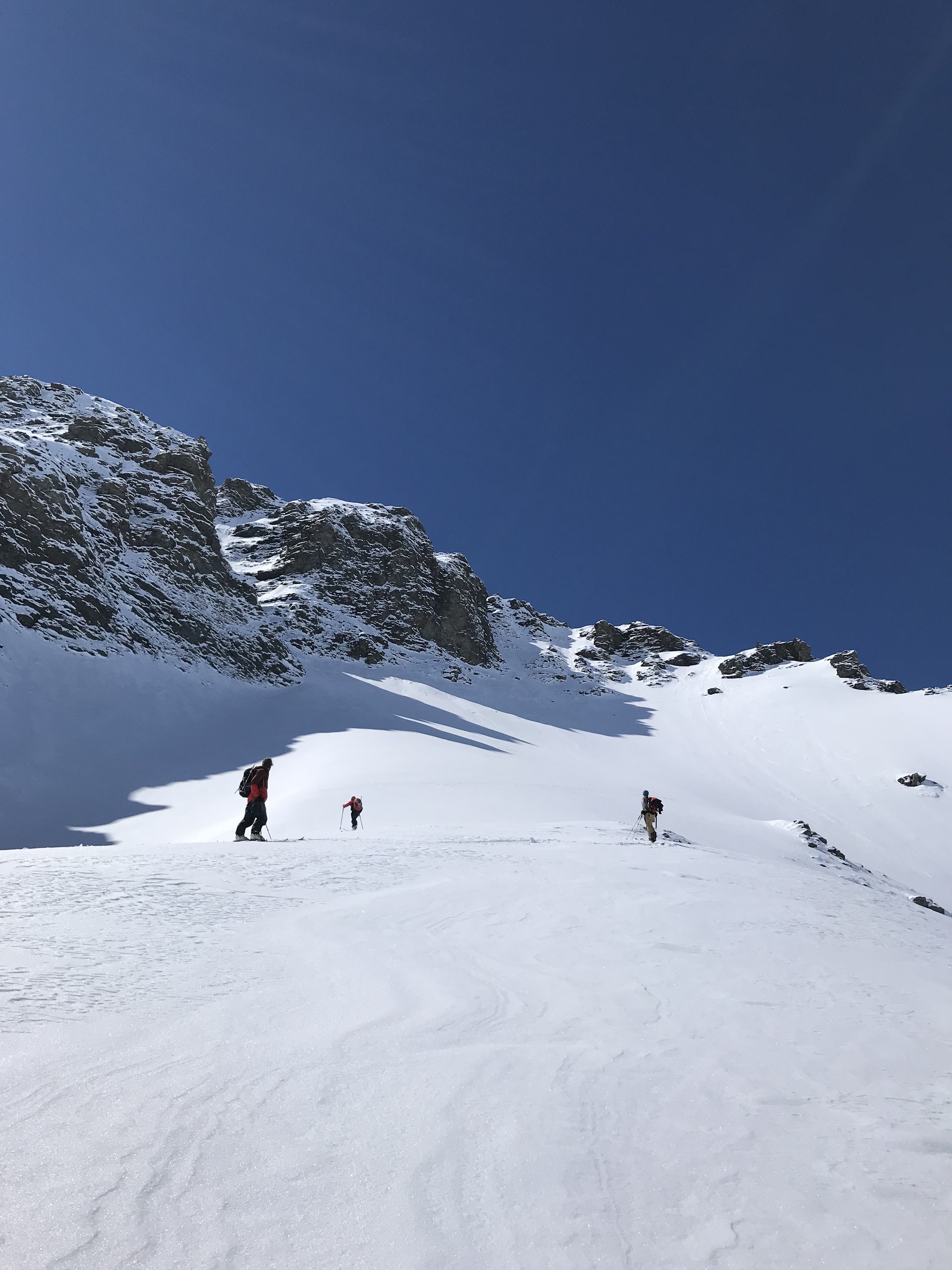 Drei Tourengeher beim Aufstieg mit Fellen an einem sonnigen Hang unter Felsbändern