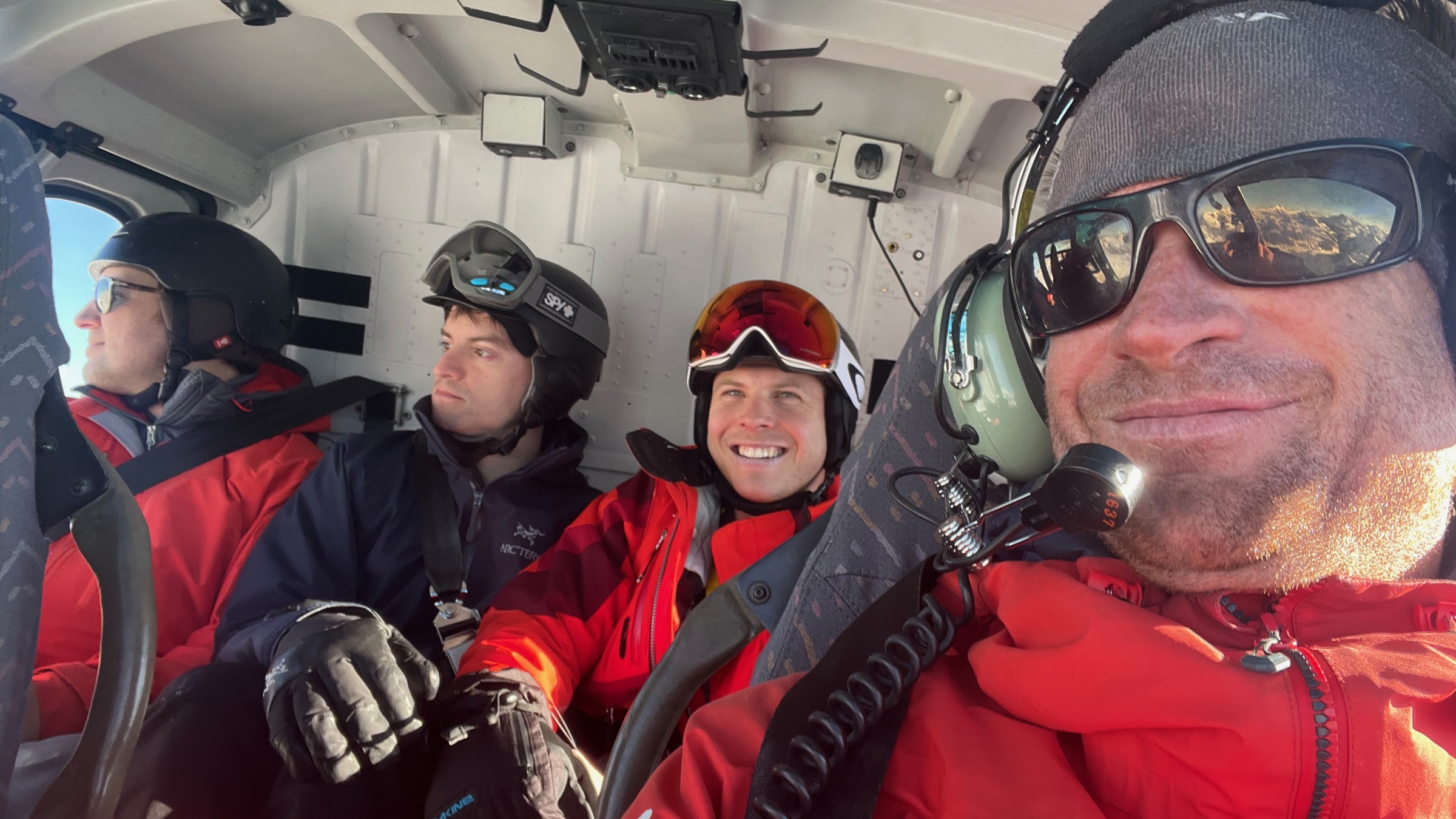 Skifahrer mit Helm in der Hubschrauberkabine vor dem Absetzen, lächelnd und mit Blick aus dem Fenster