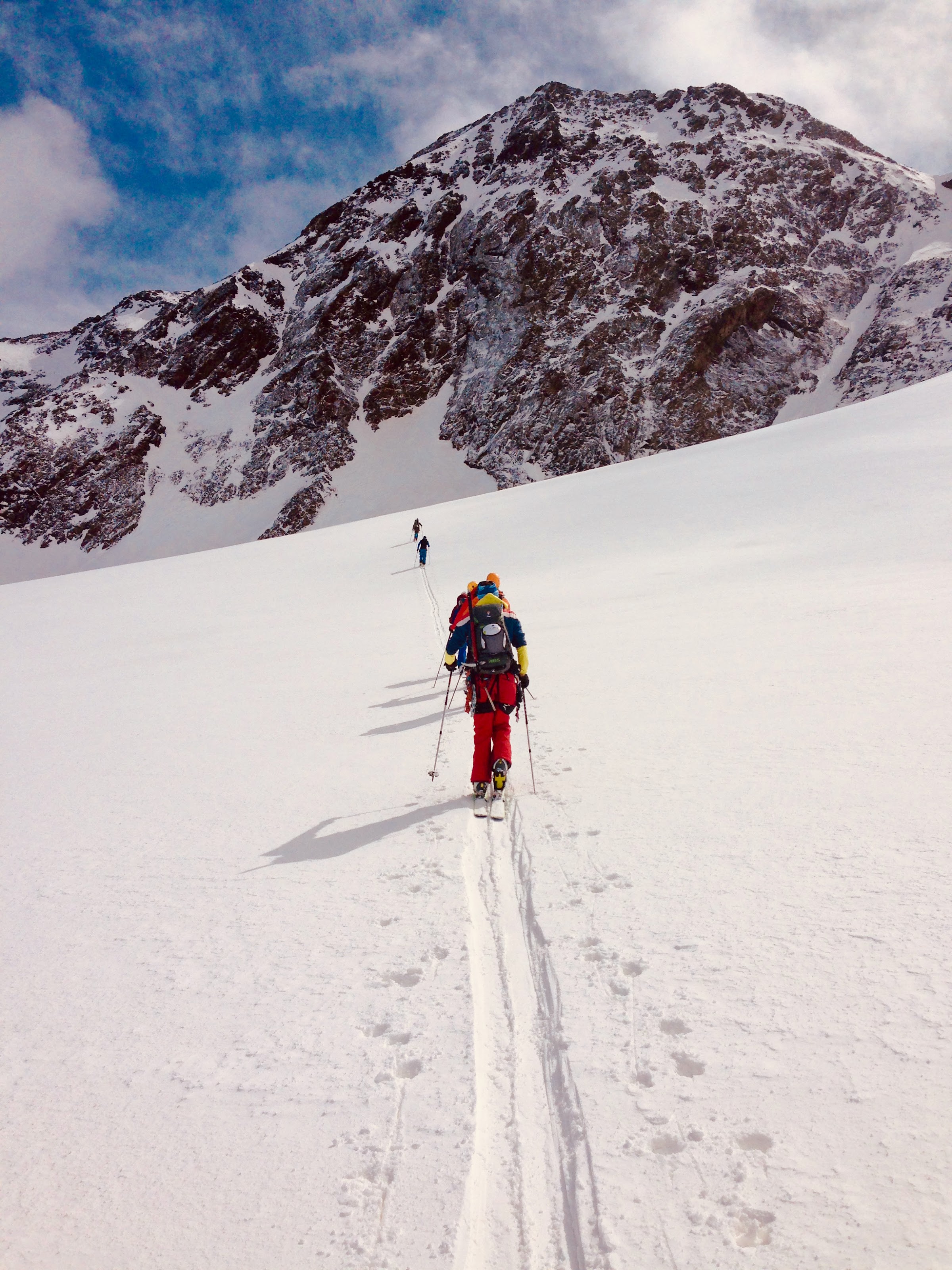 Ski tourers skinning up a straight track towards a rocky summit