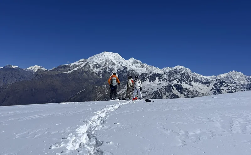 Heliskiing in Nepal: drei Skifahrer mit Helm auf einem verschneiten Plateau vor der Kette des Himalaya, tiefblauer Himmel