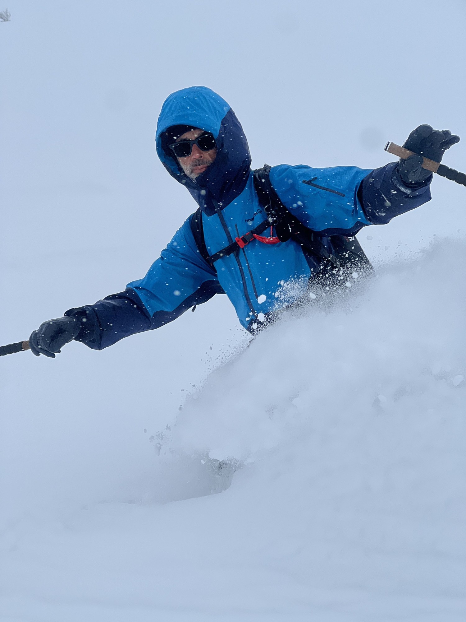 Nahaufnahme eines Skifahrers in blauer Jacke im tiefen Pulverschnee, eine Wolke trockenen Schnees in der Luft