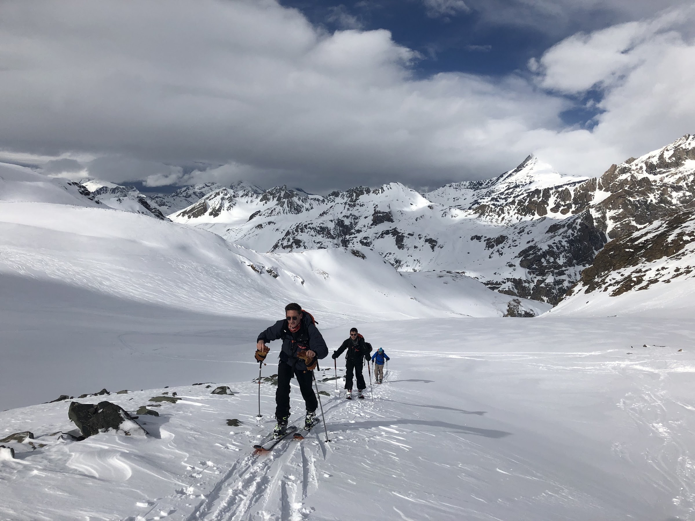 Three ski tourers skinning up a snowy valley below cloud-capped peaks