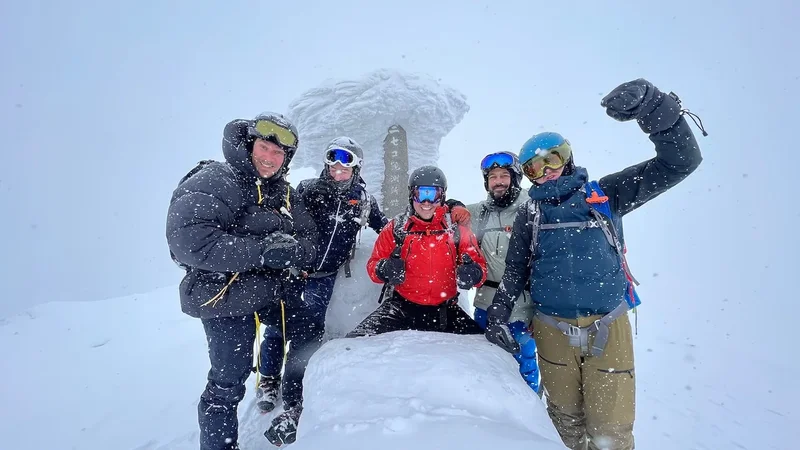 Eine glückliche Gruppe Skifahrer am Gipfel, rund um einen verschneiten Felsen