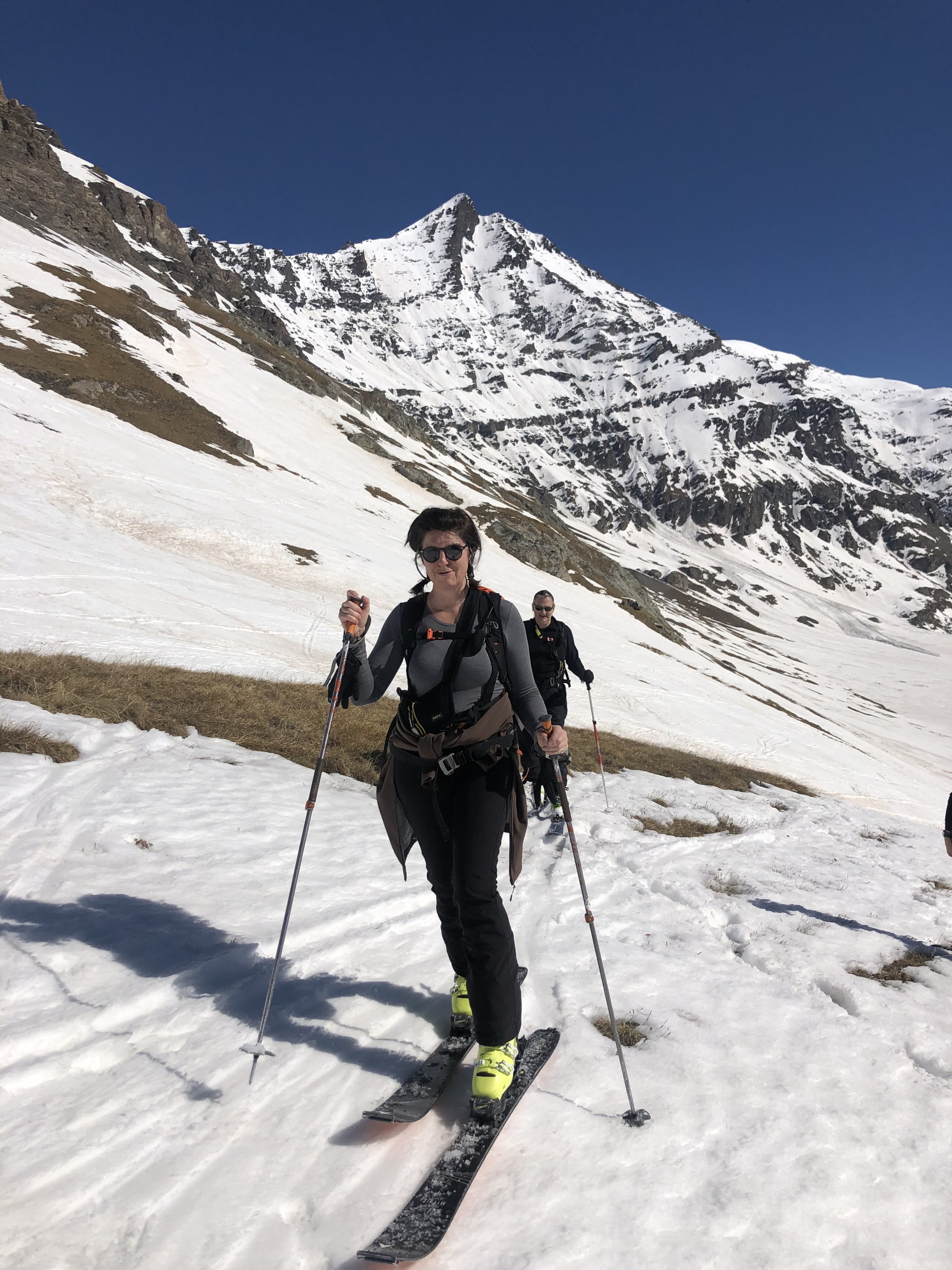 Smiling skier skinning up on spring snow, with another ski tourer behind her