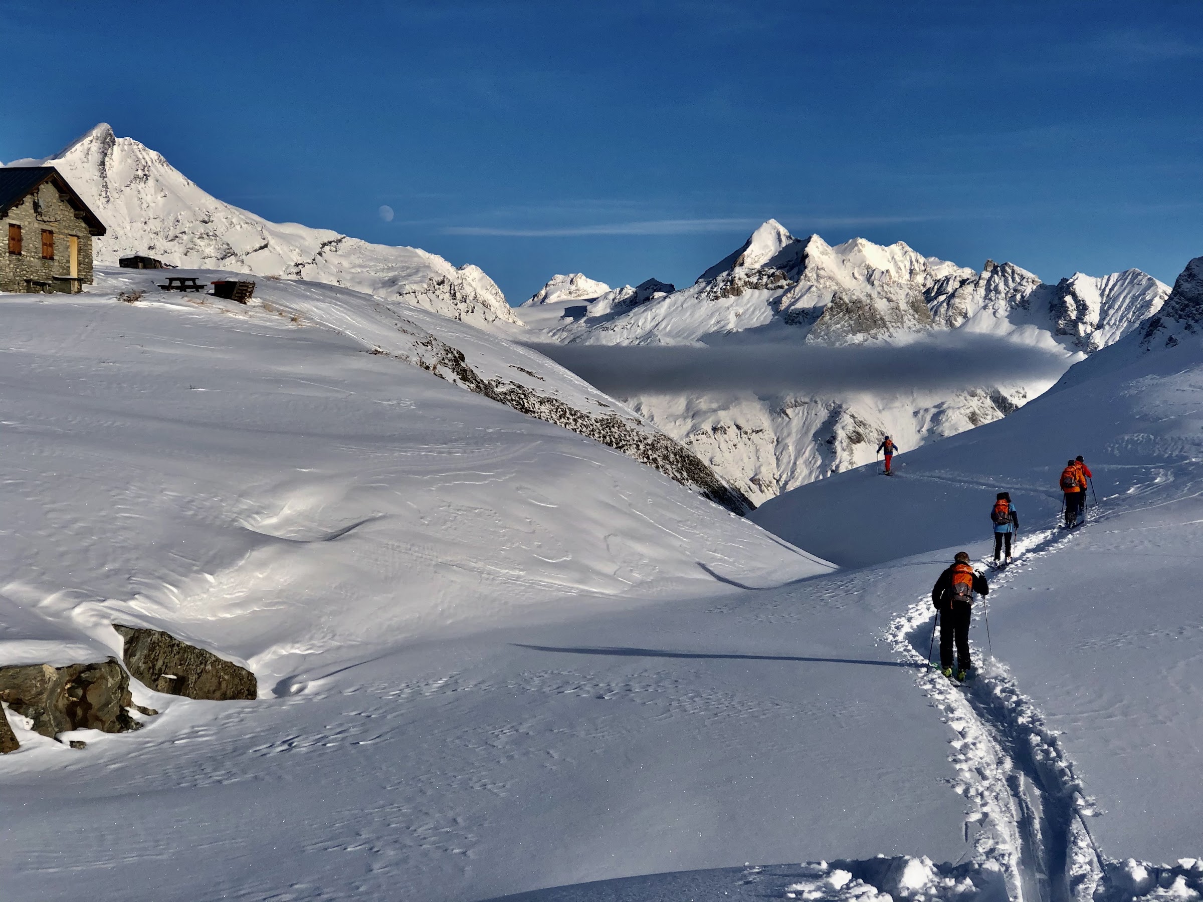 Gruppe beim Aufstieg mit Fellen in frischer Spur bei Val d'Isère, Steinhütte und Gipfel im Hintergrund