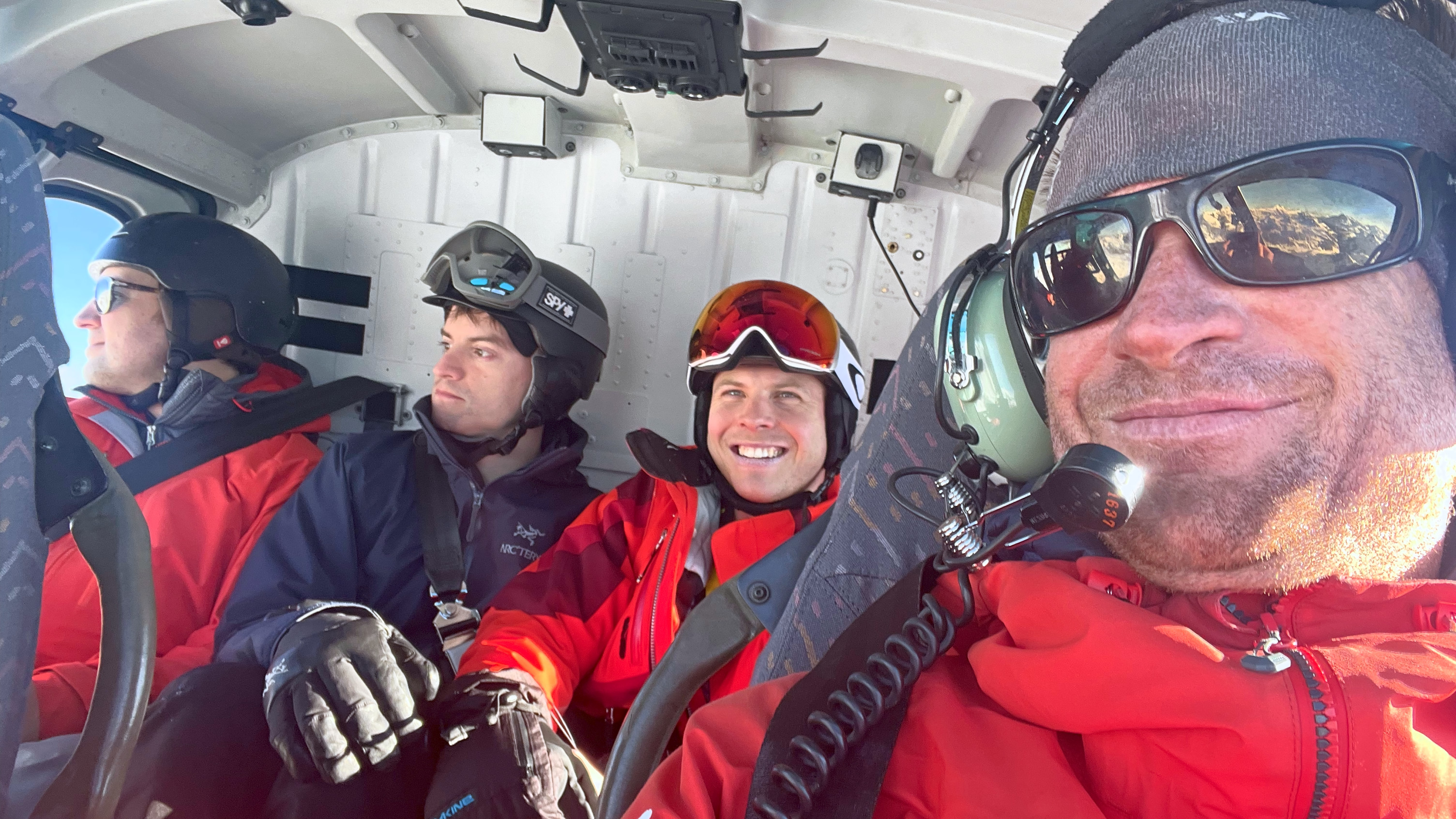 Helikopter-Transfer: lächelnde Passagiere in Skikleidung in der Kabine eines Hubschraubers im Flug, Blick aus dem Fenster