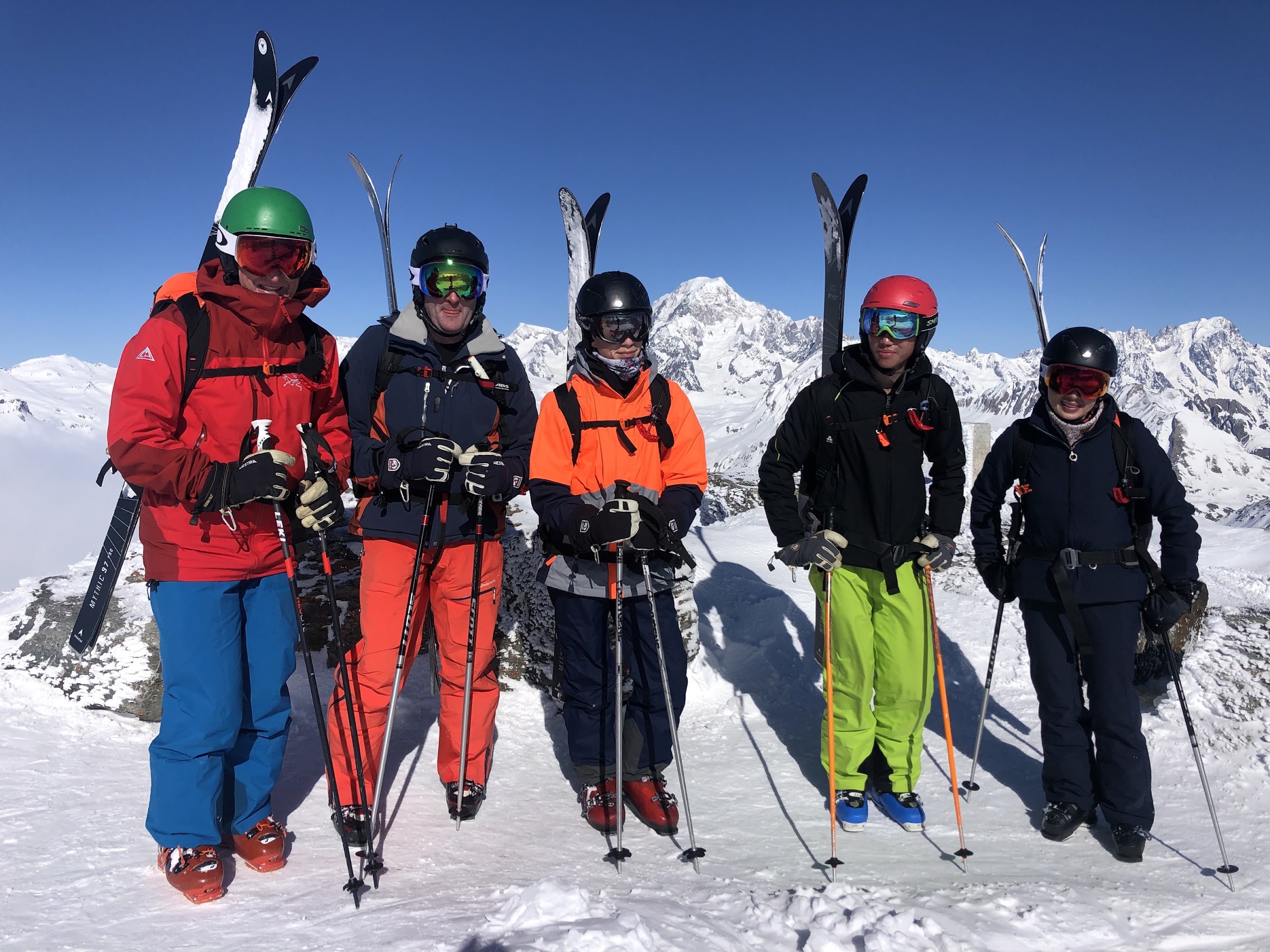 Fünf Skifahrer posieren auf einem Gipfel, Ski im Schnee, vor einer Kette hoher verschneiter Gipfel