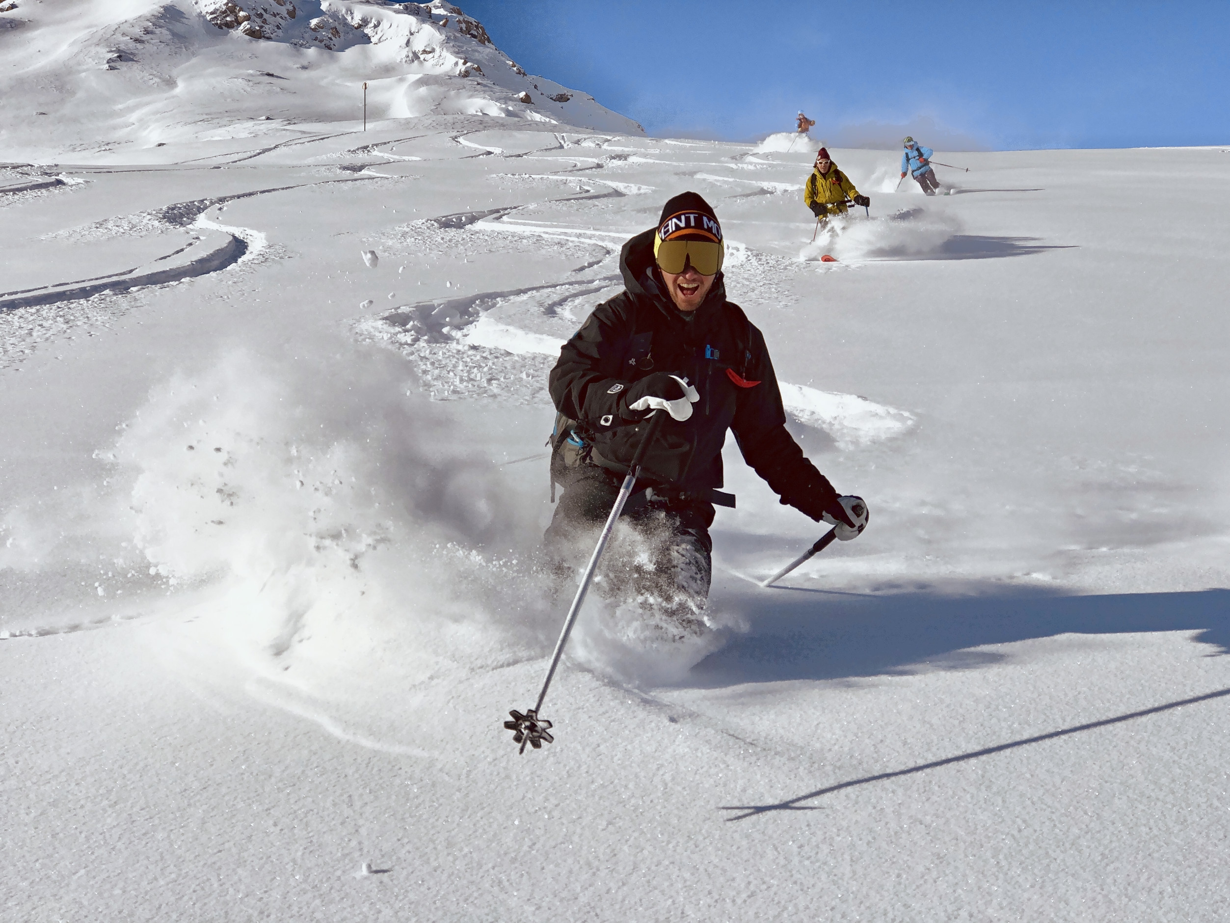 Ski school Tignes: a laughing skier in deep powder, his small group following under a deep blue sky