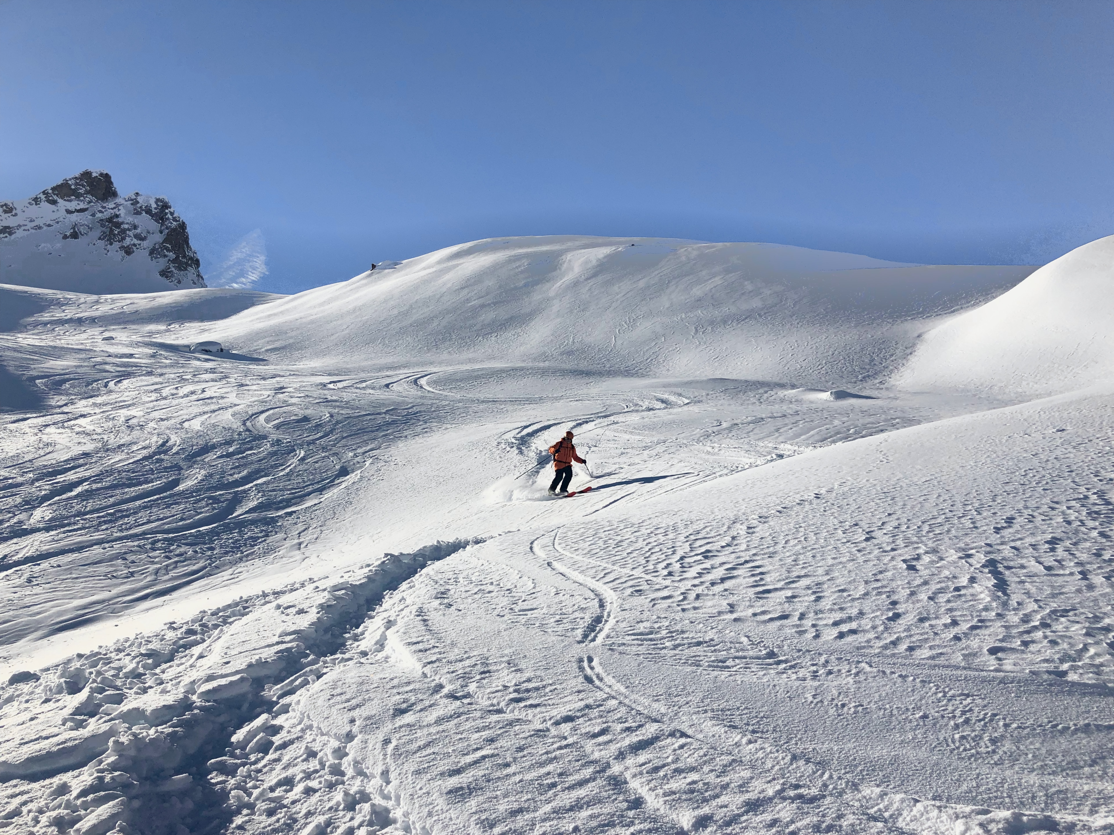 Val d'Isère ski school: a lone skier descending a wide snowy bowl under a blue sky, tracks in the snow