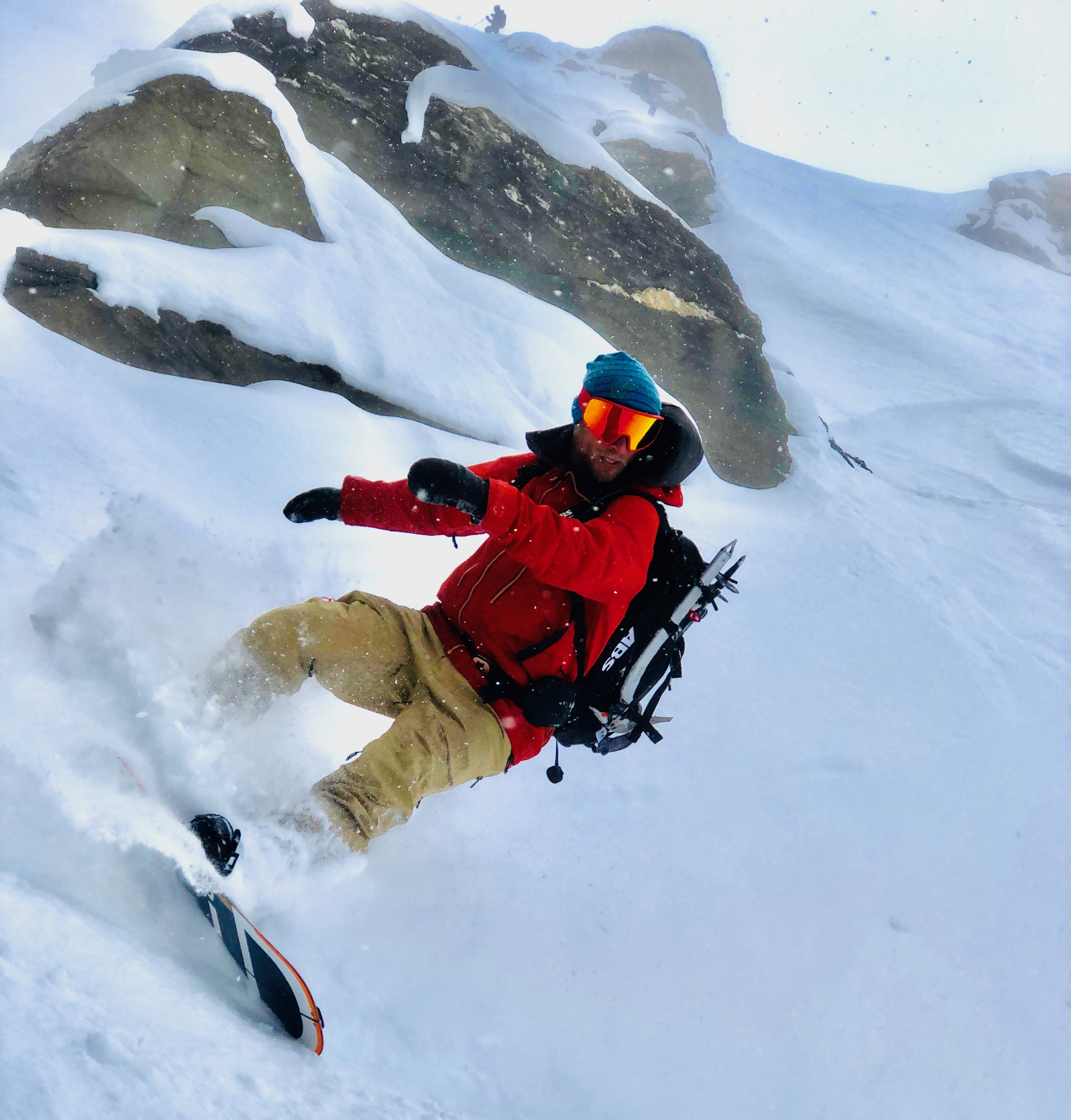 Snowboarder in roter Jacke taucht unter einem großen Felsen in den Neuschnee ein