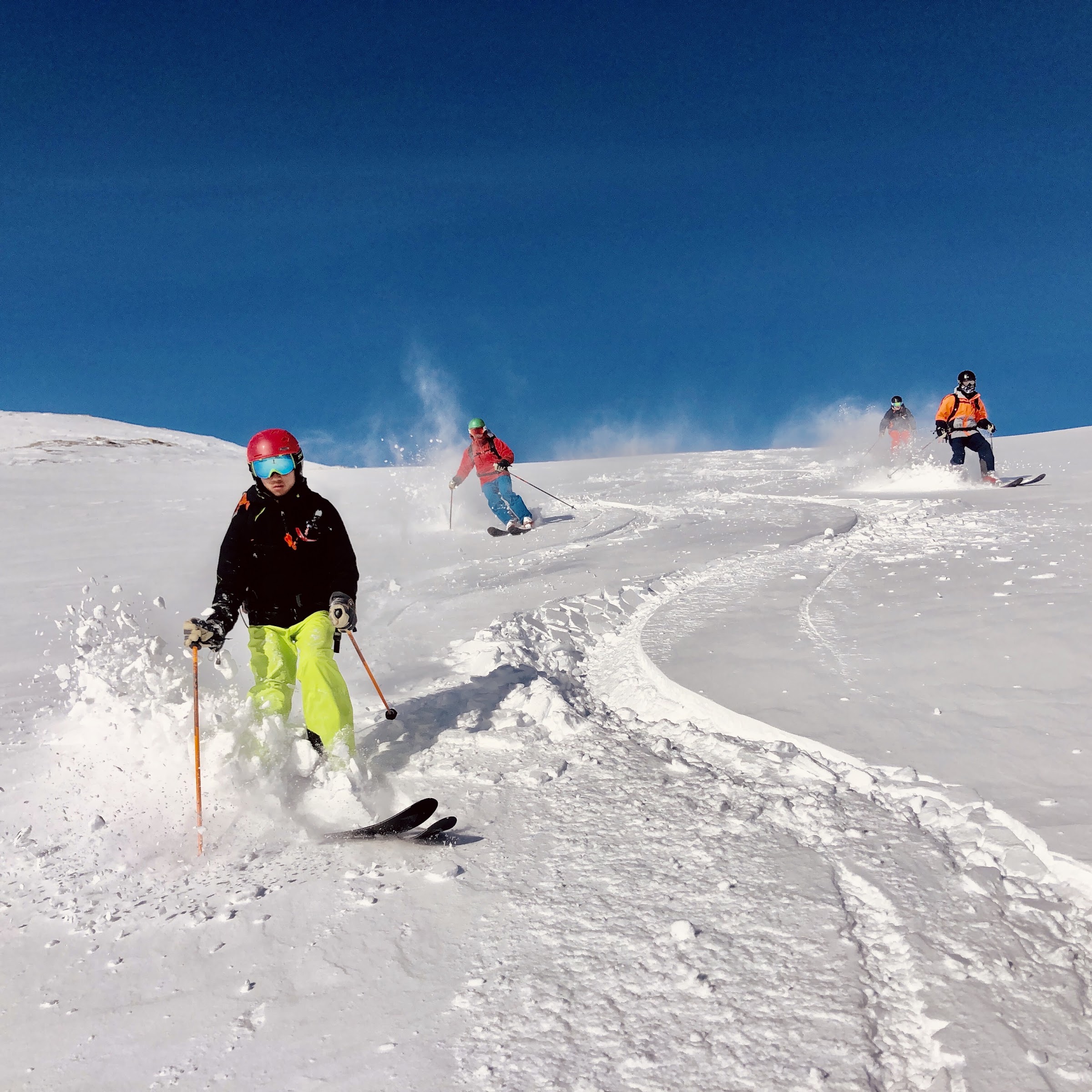 Kleine Gruppe von vier Skifahrern, die hintereinander ihre Schwünge in den Pulverschnee ziehen