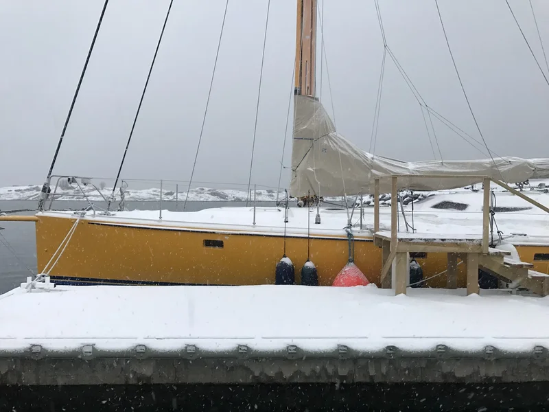 Gelbes Segelschiff am verschneiten Steg, Masten und Wanten vor klarem Himmel