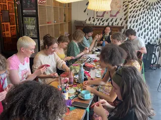 A group of people at Slow Fashion Socials, working round a table, cutting and sticking with textiles