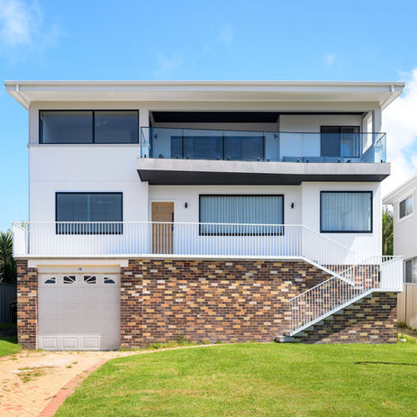 Modern two-story white house with stone facade, glass balcony, green lawn.