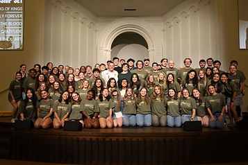 A large group of college student volunteers wearing matching t-shirts on stage.