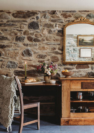 Stone wall dining nook with flowers, bread and vintage style mirror.  