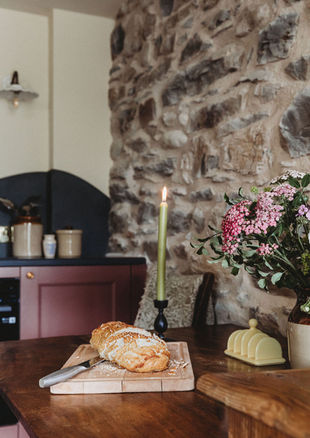Cottage kitchen with dark red units, a cloud shaped slate splash back and small wooden table designed and styled by Lisa Kay at Rural Wildings Interior Design. 