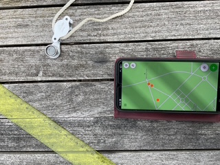 A mobile phone, ruler and hand lens on an outside table.