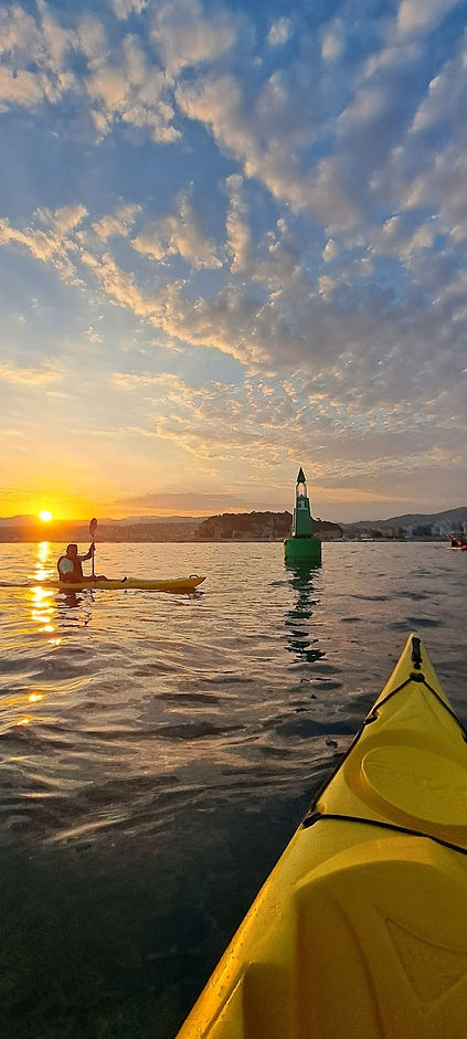 Un kayakiste pagayant en mer au coucher de soleil, avec en arrière-plan la ville de Nice et les collines environnantes.
