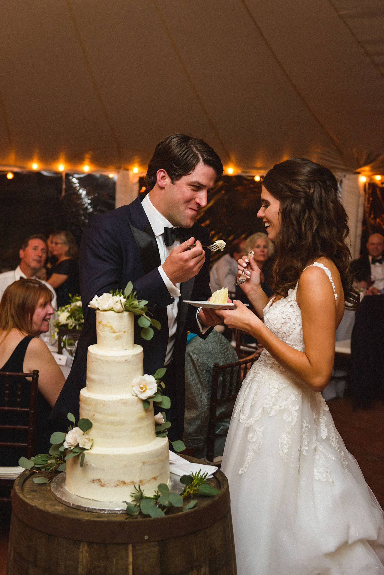 A bride and groom eat cake under a Sperry pole tent at Farm Neck Golf Club  photo by David Welch Photography