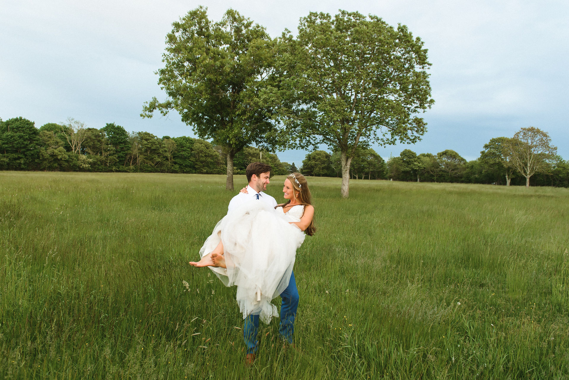 A groom carrying his bride in a field at the Martha's Vineyard Agricultural Hall in West Tisbury photo by David Welch Photography