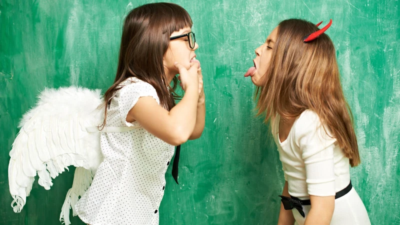 zwei Mädchen, verkleidet als Engelchen und Teufelchen zoffen sich 