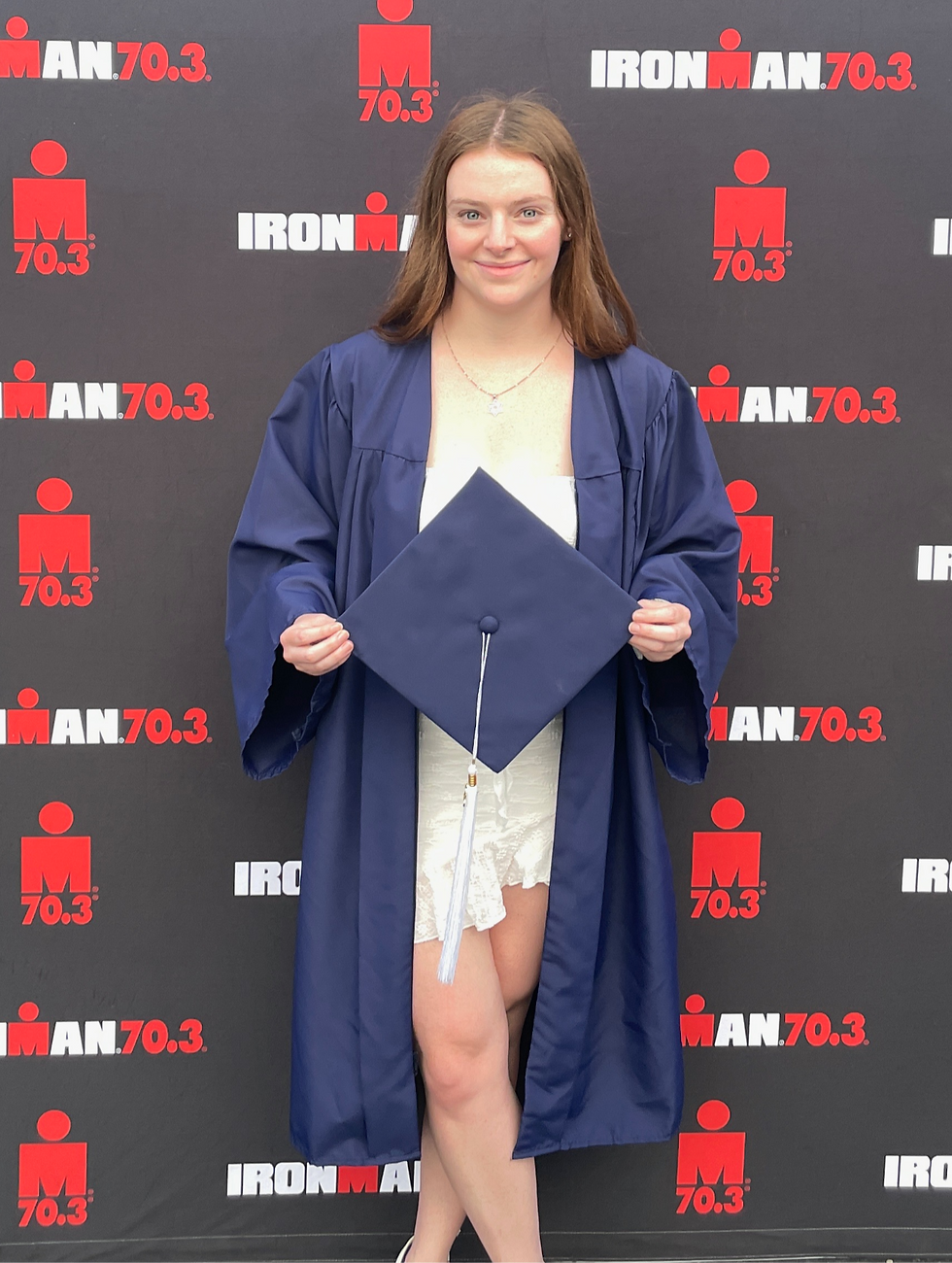 Abby wearing her graduation regalia in front of an Ironman sign