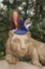 Abby graduation photo from Penn State, wearing her graduation regalia laying on top of the Penn State lion