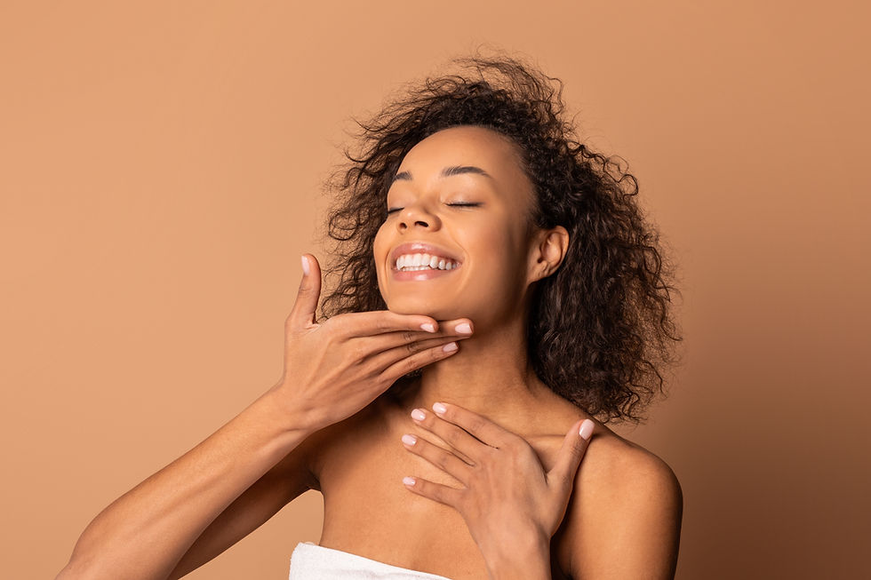 A happy African American young woman with curly hair is smiling and applying a skin care p