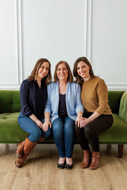 A mother and her two daughters sit together on a green tufted couch during their fall family photoshoot at an indoor studio in Dallas, TX. Image captured by Photography of Sarah Mae. 