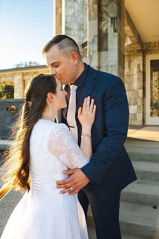 A Bride is kissed on her forehead by the groom as sunlight streams in around the two holding onto each other on the steps of the Dallas LDS Temple.