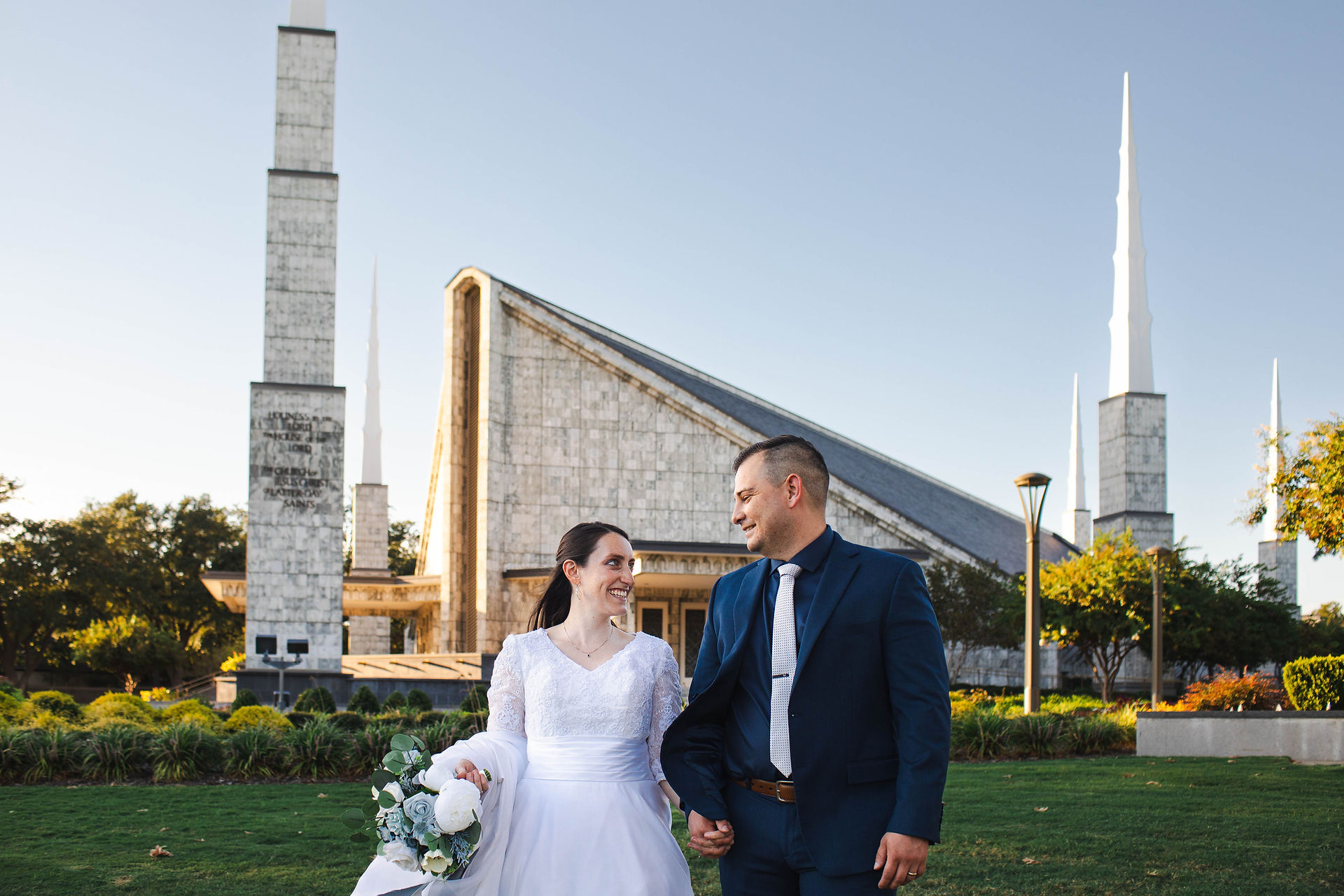 Bride and Groom hold hands and walk in front of the Dallas LDS Temple.