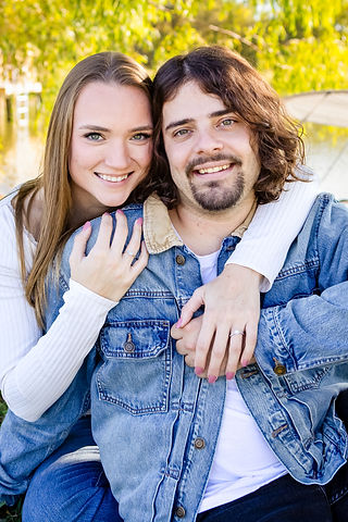 Romantic engagement photo pose of the couple cheek to cheek. The woman's arms wrapped around her fiancé's shoulders as they smile for the camera. 