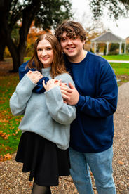A woman is leaning back against her husband on a cobblestone path at the A W Perry Homestead. His arms are wrapped around her and the two of them are smiling into the camera.